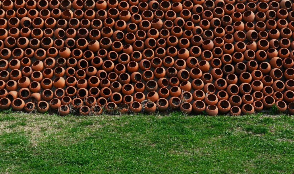 Dicht an dicht gestapelte orangefarbene Tonamphoren vor einer Rasenfläche