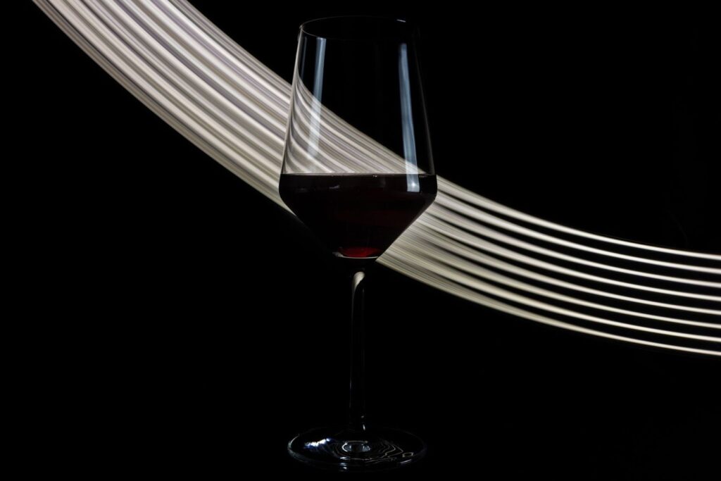 Bauchiges Weinglas mit Rotwein vor geschwungenen Lichtstreifen
